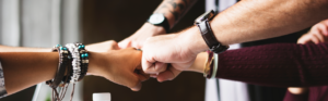 Close-up of a group of people joining hands in a fist bump gesture, symbolizing teamwork and collaboration.