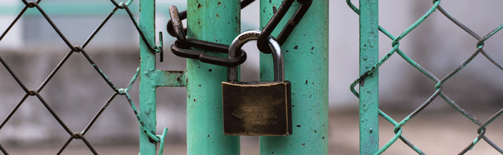 Close-up photo of a metal gate secured with a padlock and chain, symbolizing security or restricted access.