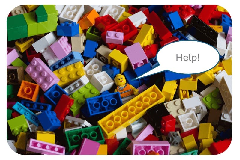 A pile of colorful LEGO blocks with a LEGO minifigure in the middle holding a speech bubble that says “Help!”