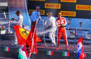 Formula One drivers celebrating on a podium spraying champagne after a race victory.